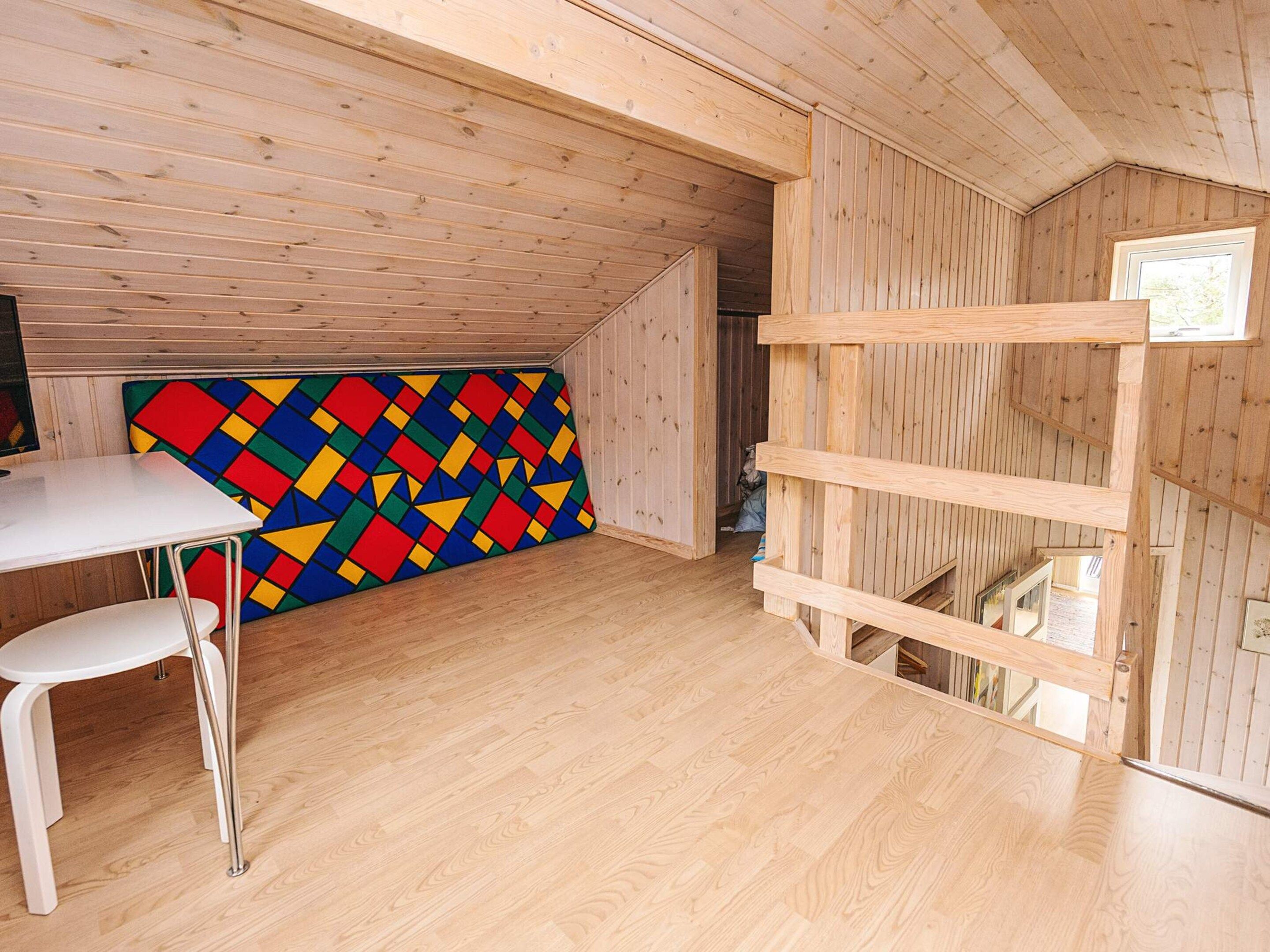 A room with a wooden ceiling, a white table, a colorful geometric wall, and a white chair.