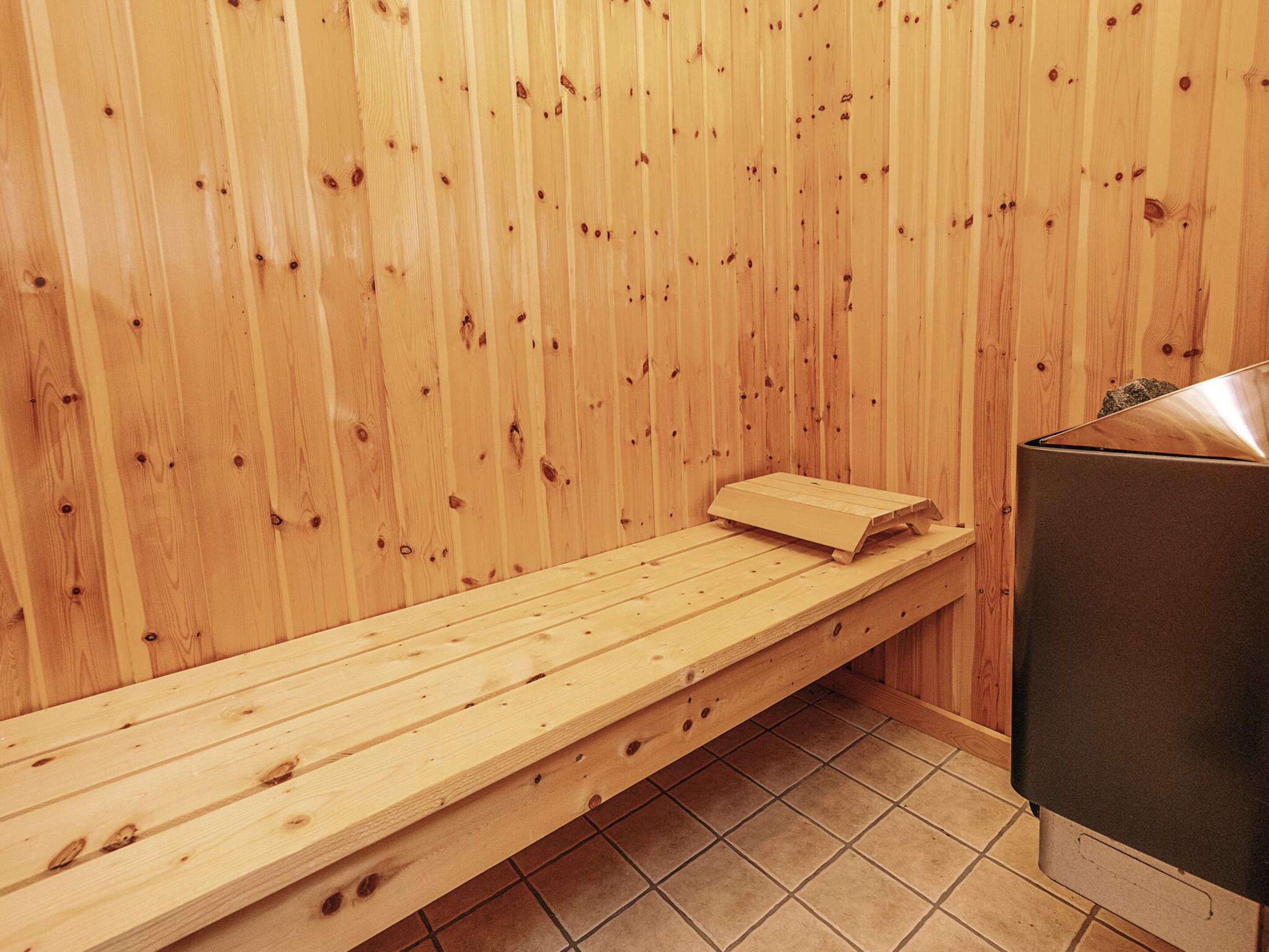 Banco de sauna de madera con una toalla, calentador de sauna y suelo de baldosas.