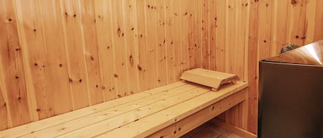 A wooden sauna bench with a towel, a sauna heater, and a tiled floor.