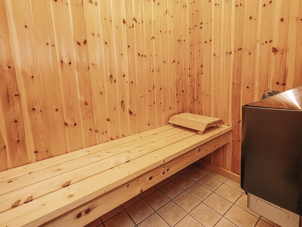 A wooden sauna bench with a towel, a sauna heater, and a tiled floor.