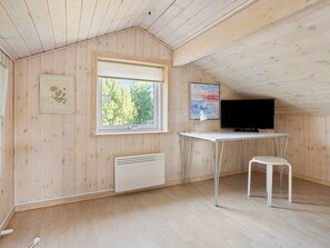Ein Zimmer mit Holzwänden, einem Fenster, einem Heizkörper, einem Schreibtisch mit Fernseher und einem Stuhl.