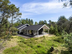 Ein modernes Haus mit einer großen Terrasse, umgeben von dichtem Wald.