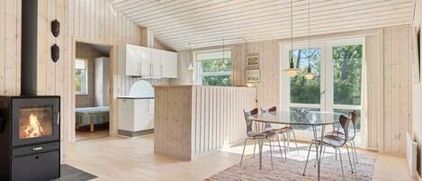 A spacious kitchen with wooden walls and a large island, a dining area with chairs, and a fireplace.