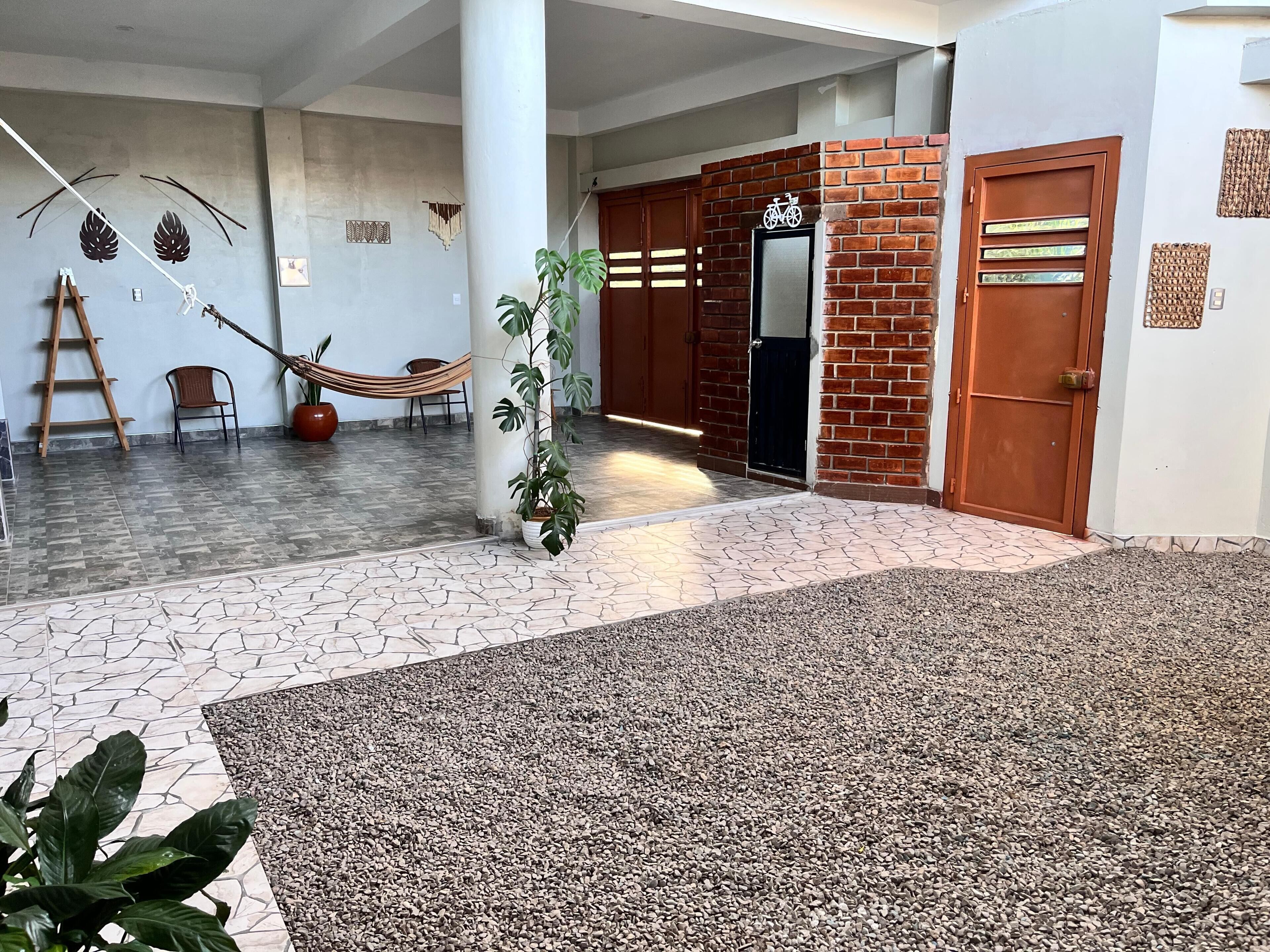 A spacious indoor area with a tiled floor, a hammock, a potted plant, and a brick wall with a door.