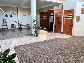 A spacious indoor area with a tiled floor, a hammock, a potted plant, and a brick wall with a door.