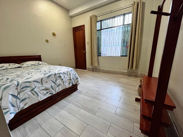 A bedroom with a bed, a wooden dresser, a window with curtains, and a door.