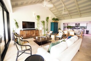 A spacious living area with a sofa, chairs, a coffee table, and a TV. There are plants and a cabinet in the background. - Luxury on the ocean, Teeth of the Dog Golf view (La Romana,)