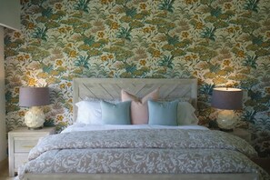 Ein Schlafzimmer mit floraler Tapete, einem Bett mit gemusterten Betttextilien und zwei Nachttischlampen.