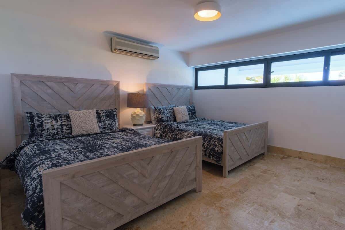 Quarto com duas camas, uma janela e um aparelho de ar condicionado.