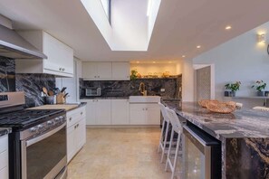 Eine moderne Küche mit Oberlichter, Marmorarbeitsplatten und einer zentralen Kochinsel mit Barhocker.