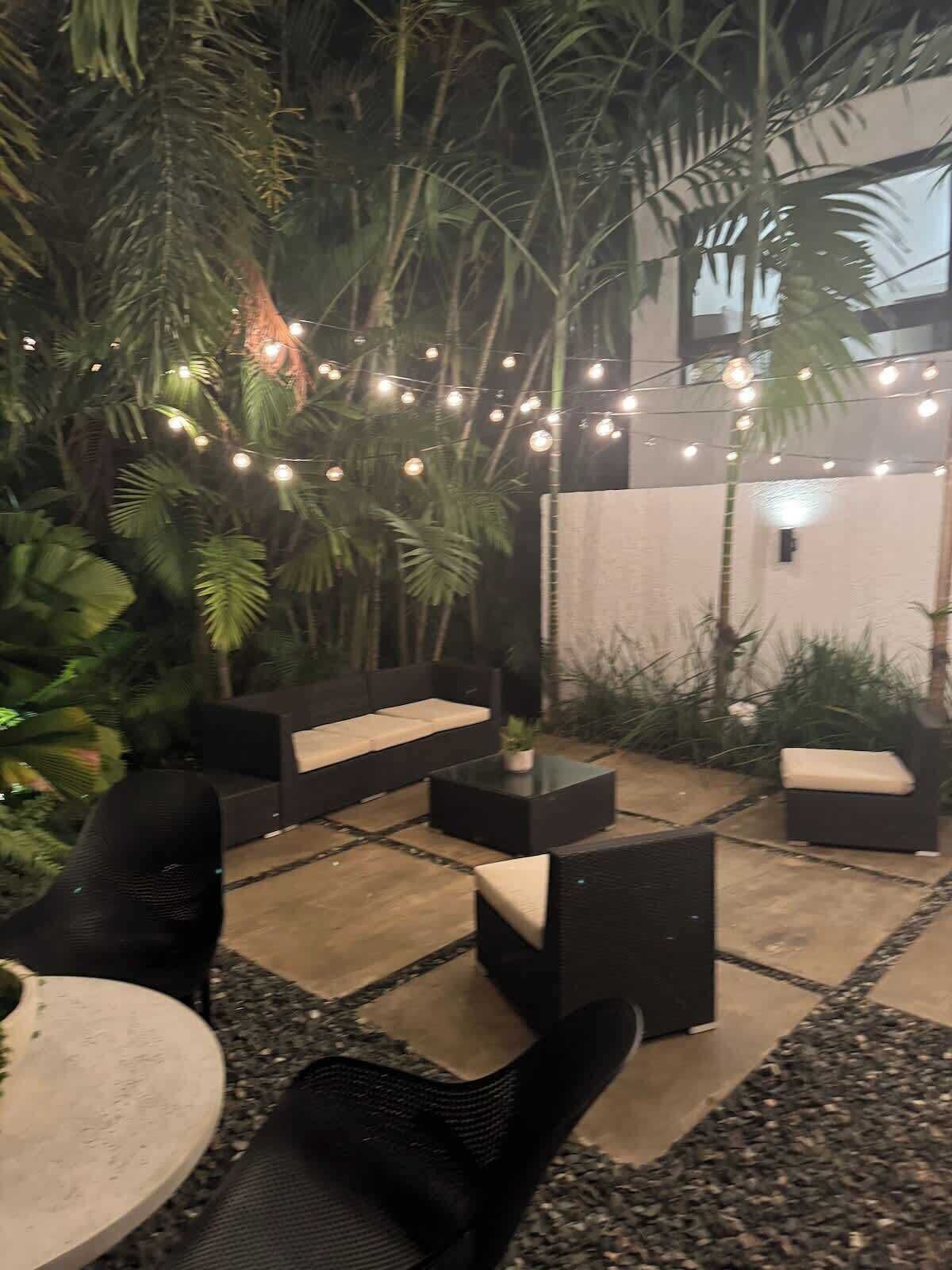 Un espace extérieur aménagé avec des meubles noirs et des guirlandes lumineuses.