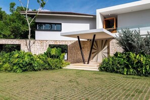 Uma casa moderna com fachada de pedra, área de estar coberta ao ar livre e vegetação exuberante.
