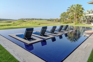 Piscina com espreguiçadeiras e vista para um campo de golfe.