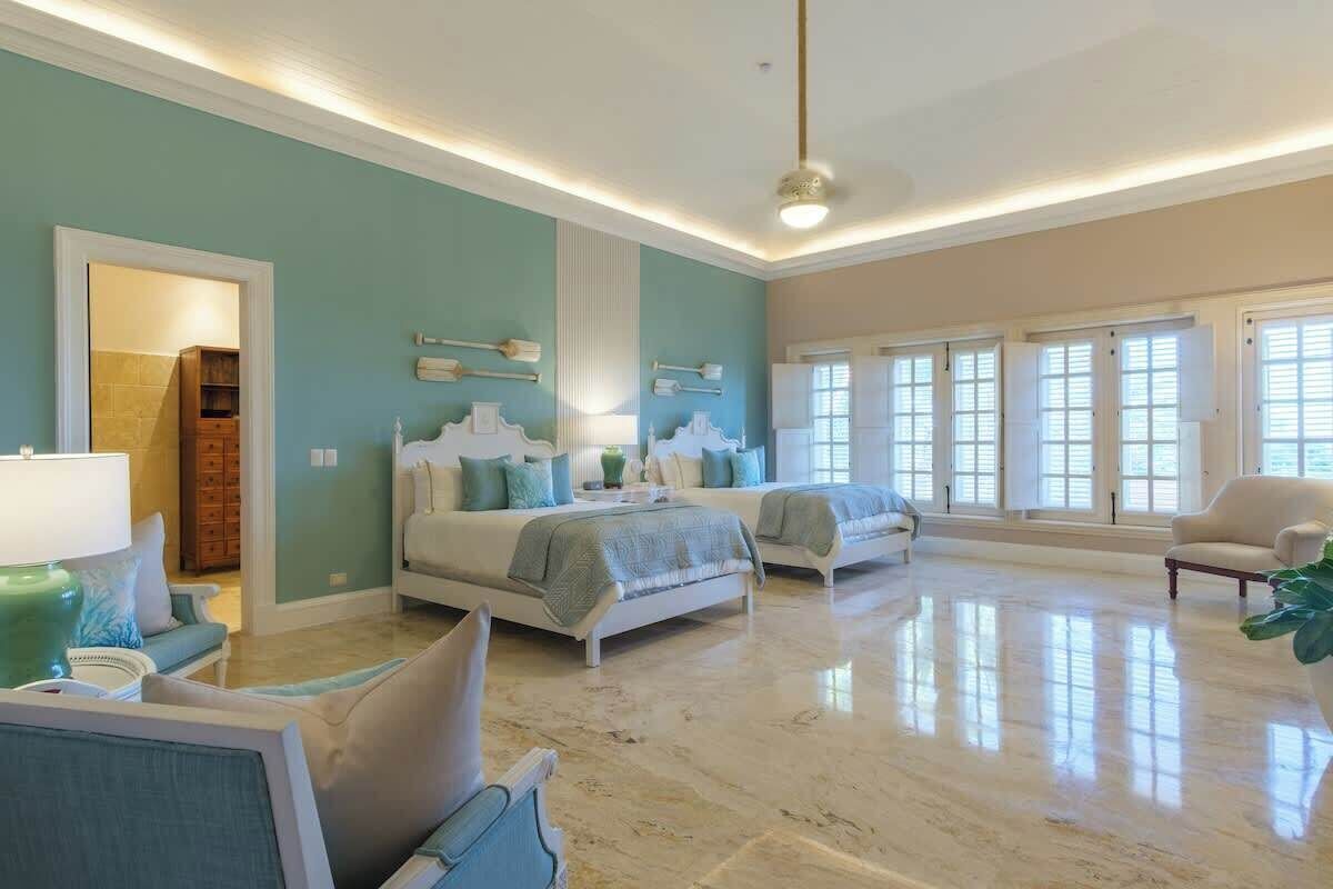 A spacious bedroom with two beds, a sitting area with a chair and a table, and a bathroom with a shower and a toilet.