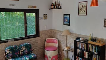 A room with a sofa, a small table, a bookshelf, and a window with a view of greenery.