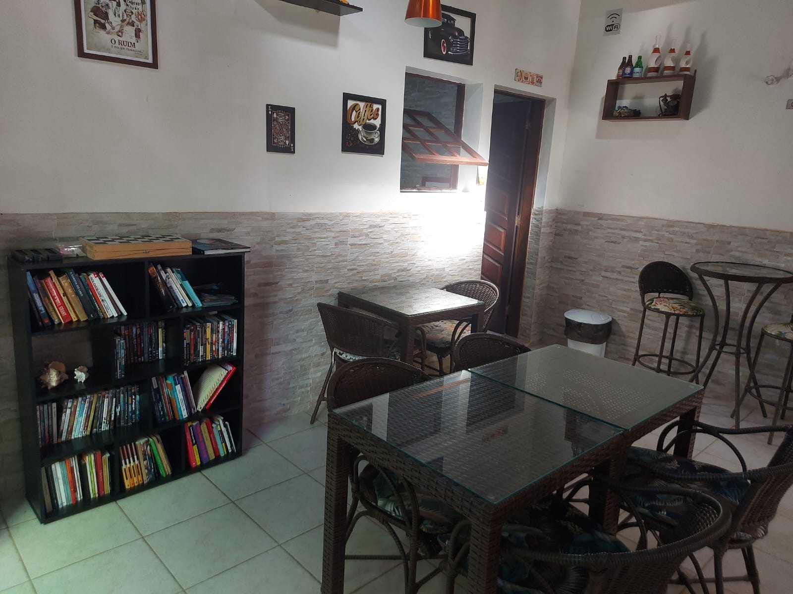 Una habitación con una mesa de vidrio, sillas de mimbre, una estantería y una pequeña zona de bar.
