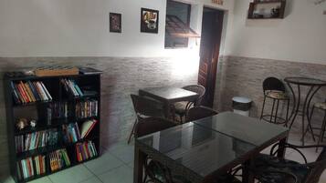 Una habitación con una mesa de vidrio, sillas de mimbre, una estantería y una pequeña zona de bar.