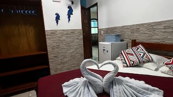 A hotel room with a bed, a TV, a fan, and a wall with decorative fish.