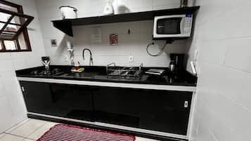 A kitchen with a black countertop, white tiles, a microwave, a blender, and a red rug.