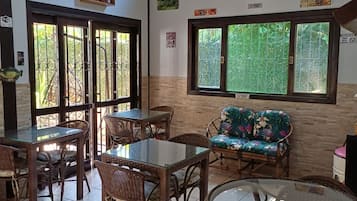 A room with a glass table, wicker chairs, a sofa, and a window with a view of greenery.