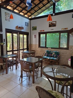 A room with a glass table, wicker chairs, a sofa, and a window with a view of greenery. - Azul del Mar (Ilha Grande)