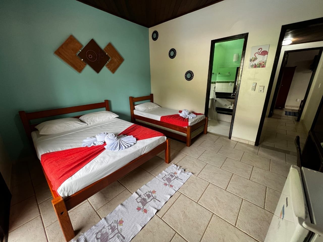 A room with two wooden beds, a kitchenette, and a bathroom visible through an open door.
