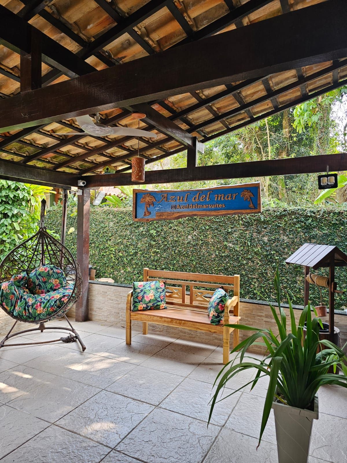 Un área de estar al aire libre con un banco de madera, una silla colgante, un letrero que dice 'Azul del mar' y una planta en maceta.