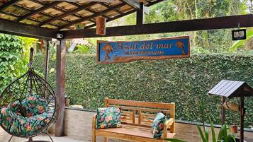Un área de estar al aire libre con un banco de madera, una silla colgante, un letrero que dice 'Azul del mar' y una planta en maceta.