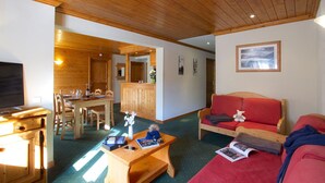 Ein gemütliches Zimmer mit Holzboden, einem Essbereich mit Holztisch und -stühlen, einem roten Sofa und einem Fernseher.