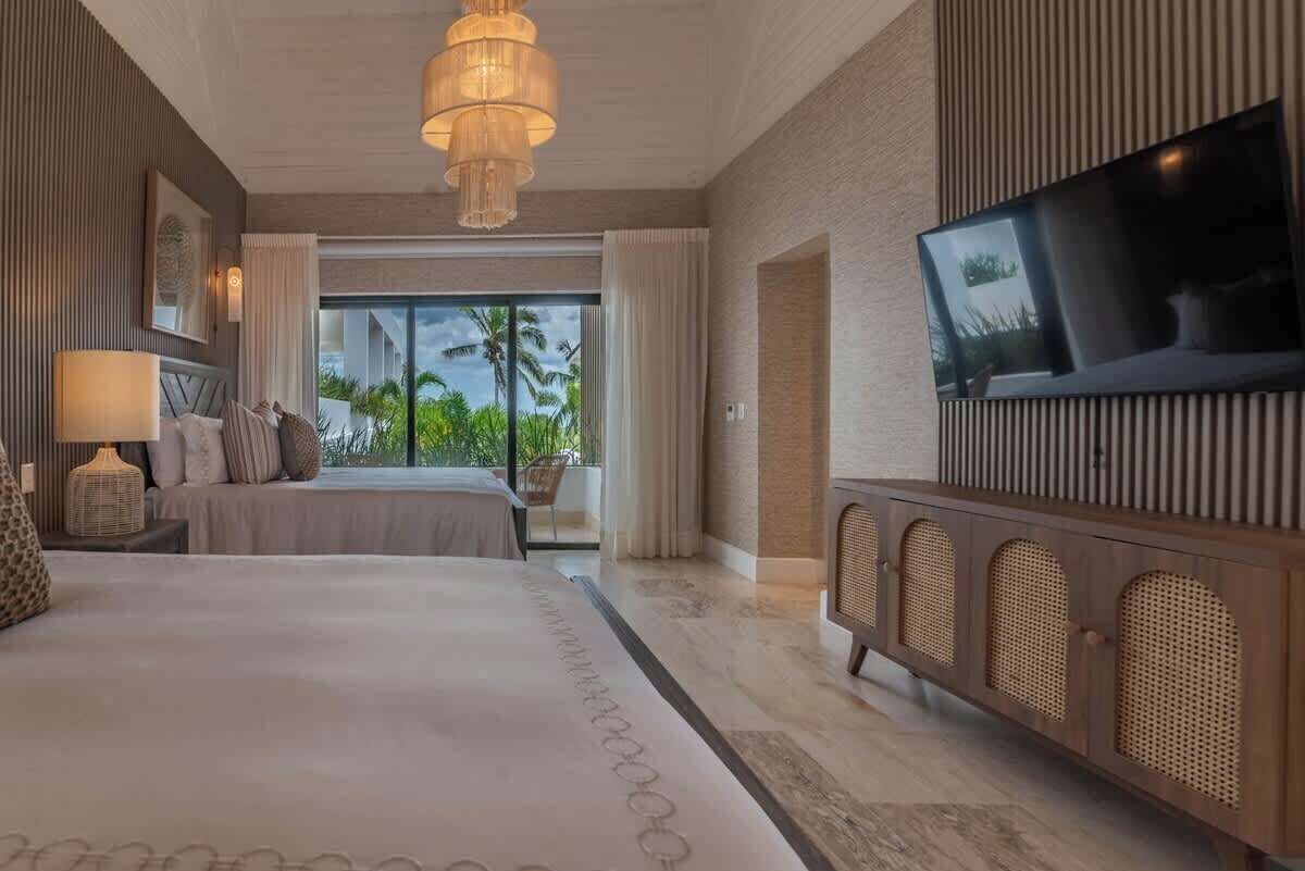 Une chambre d’hôtel dotée d’un grand lit, d’une télévision, d’un balcon offrant une vue sur les palmiers et présentant un design moderne.