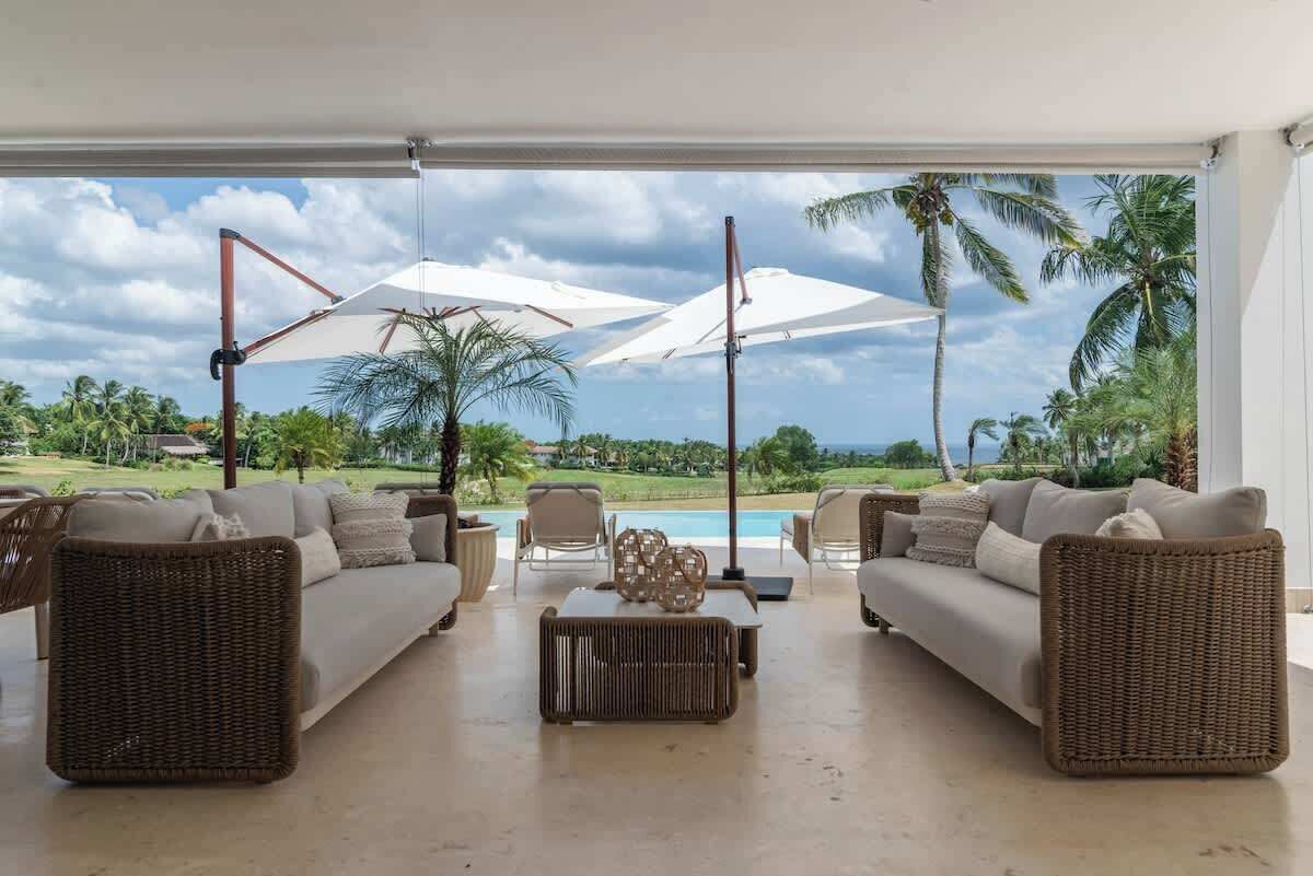 A spacious living area with a pool view, furnished with wicker sofas and a coffee table.
