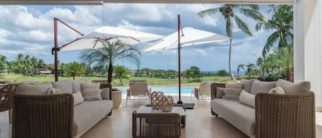 A spacious living area with a pool view, furnished with wicker sofas and a coffee table.
