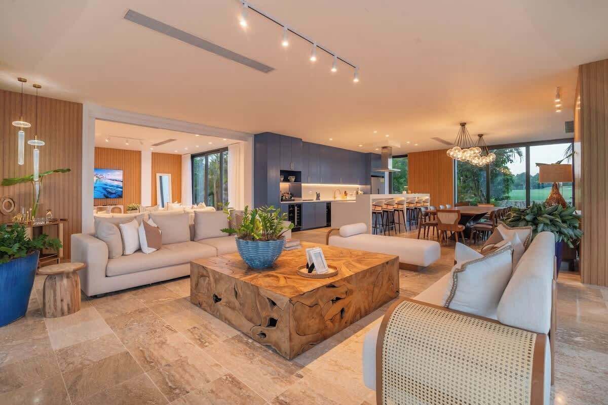 A modern living room with a large wooden coffee table, a sofa, and a dining area with a bar.