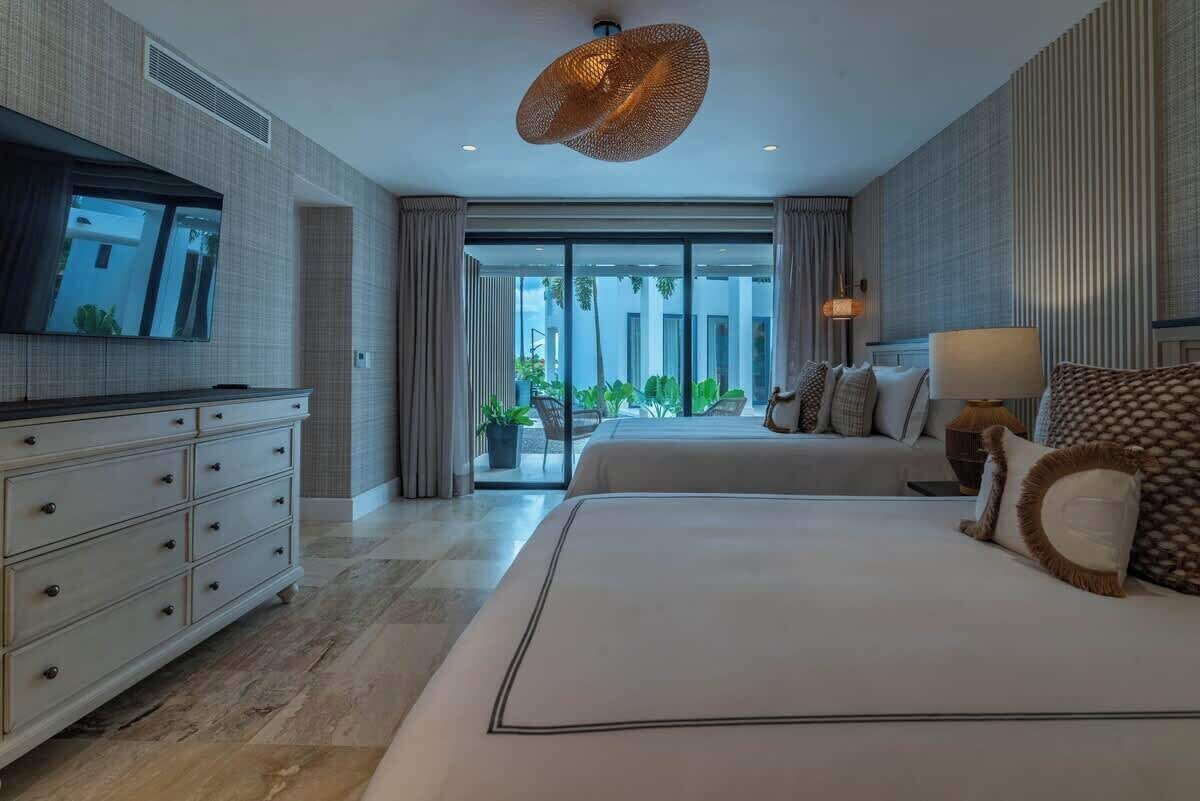 A modern hotel room with a large bed, a television, a dresser, and a view of the outdoors.
