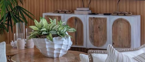Ein Wohnzimmer mit einem großen Flachbildfernseher an einer Holzwand, einem runden Holztisch mit einem Blumentopf und einem weißen Sofa.