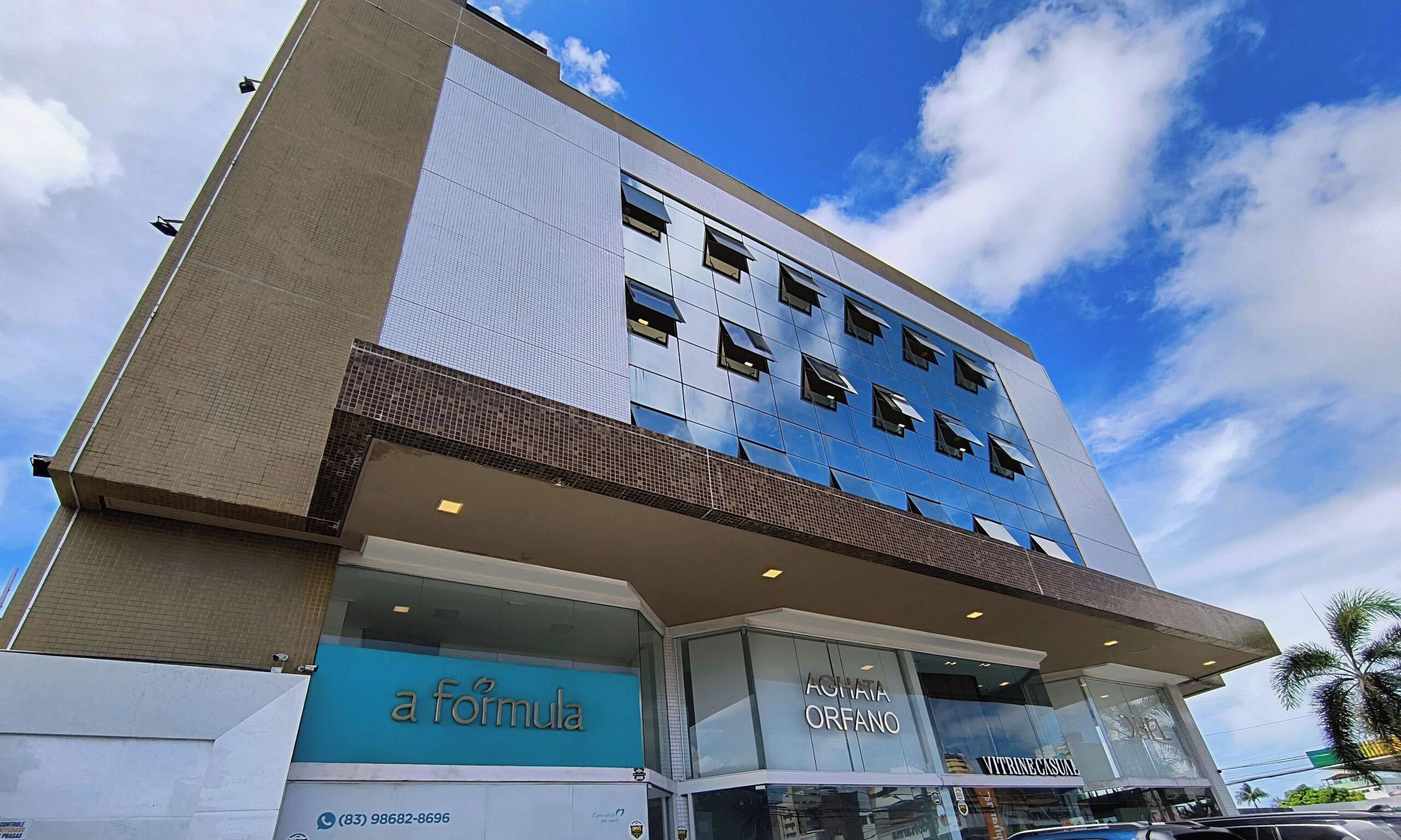 A multi-story building with a modern architectural design, featuring a mix of glass and metal facades, and storefronts for businesses like 'a formula' and 'AGHATA ORFANO'.