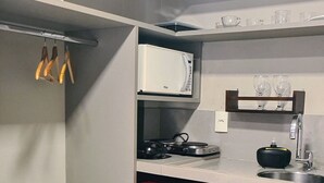 A compact kitchen with a refrigerator, stove, sink, and a red cabinet. - Flats Uno - By EasyHost (João Pessoa)