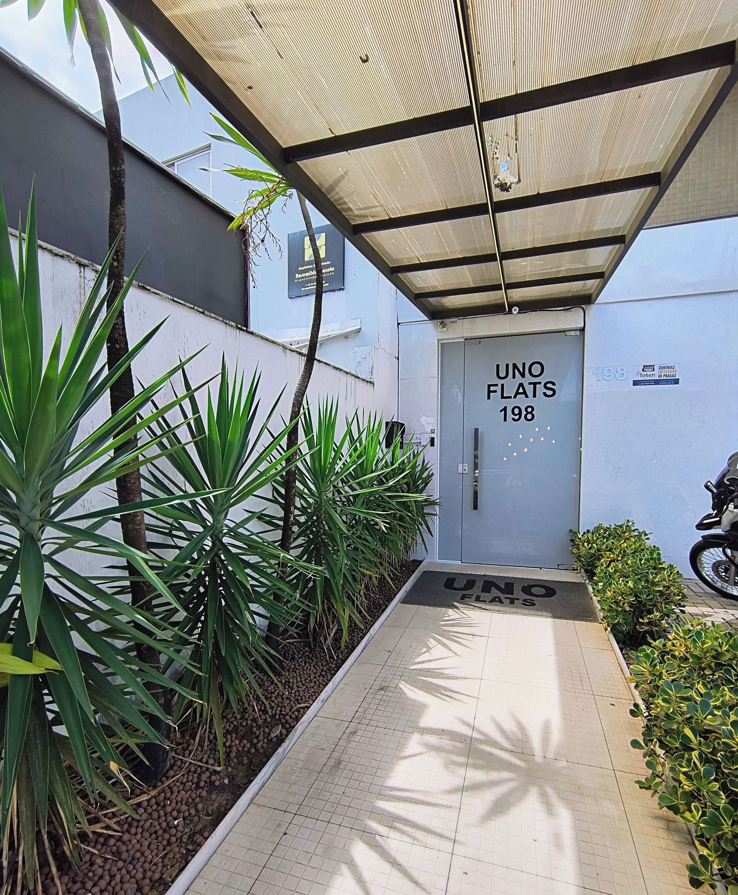 A gated entrance with a sign reading 'UNO FLATS 198' and a motorcycle parked outside.