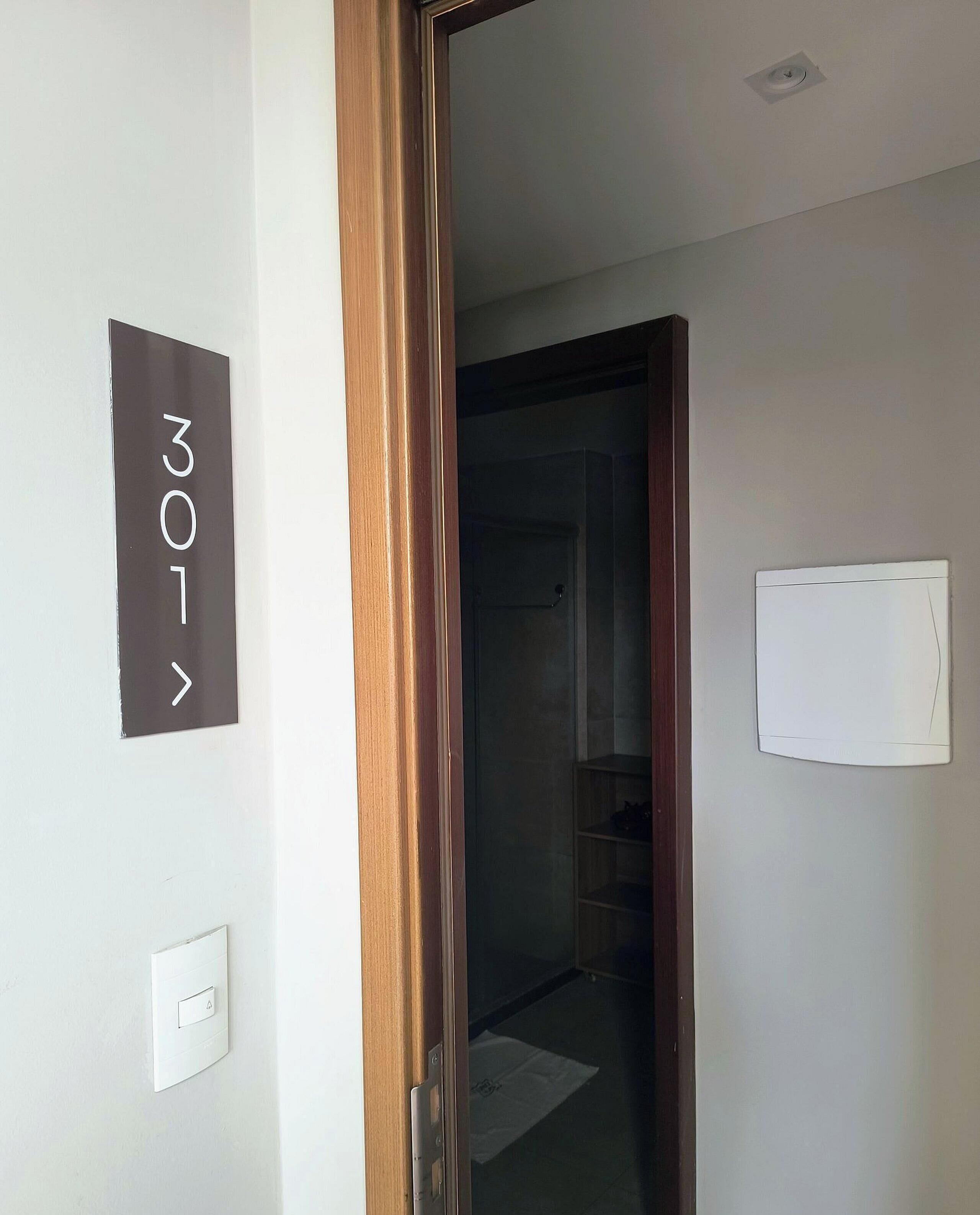 A room with a door leading to another space, a wall-mounted light switch, and a sign with the number '301'.