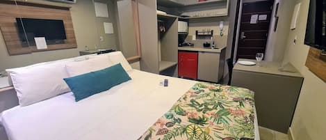 A hotel room with a bed, a desk, a kitchenette, and a bathroom.