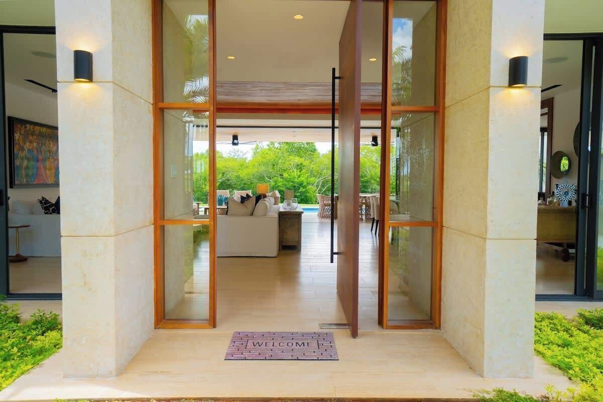 A modern entrance with a glass door, a welcome mat, and a view of an interior living space with furniture.