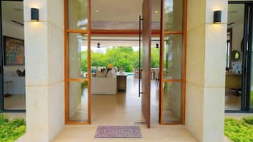 A modern entrance with a glass door, a welcome mat, and a view of an interior living space with furniture.