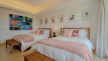A hotel room with two beds, a bench, a painting, and framed pictures on the wall.