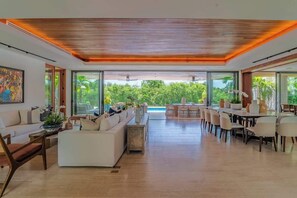 A spacious living area with a large dining table, sofas, and a view of a swimming pool.