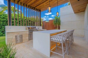 Cocina exterior con una parrilla, taburetes de bar y vistas al cielo.
