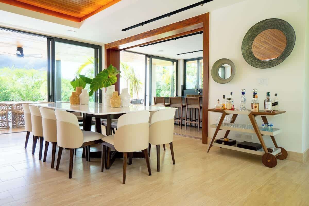 A dining area with a round table, chairs, and a bar cart with bottles.