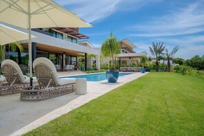Una casa moderna con piscina, mobiliario exterior y un césped bien cuidado.