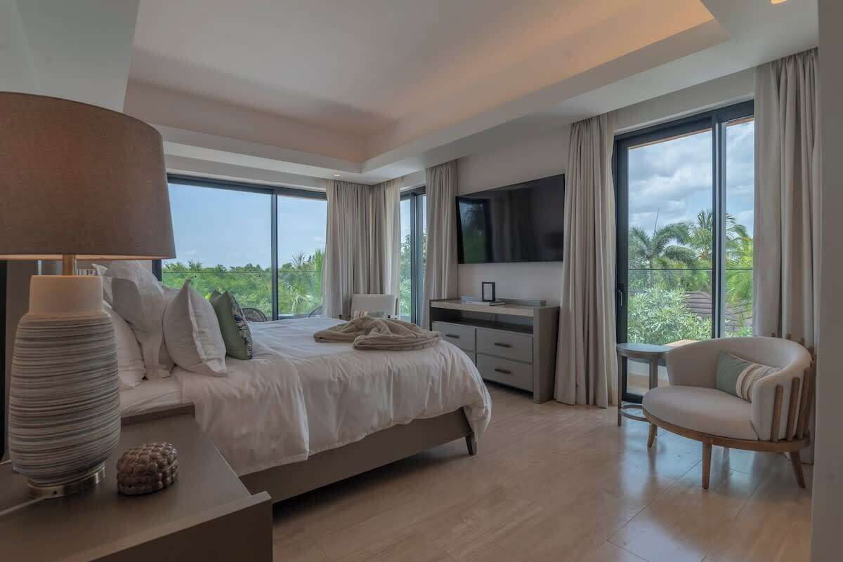 A modern bedroom with a bed, bedside table, lamp, TV, and a chair.