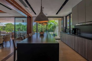Cocina moderna con una isla central, ventanas amplias y un comedor con sillas.