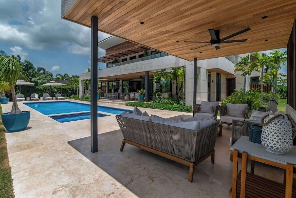 A modern outdoor living area with a pool, lounge chairs, and a ceiling fan.